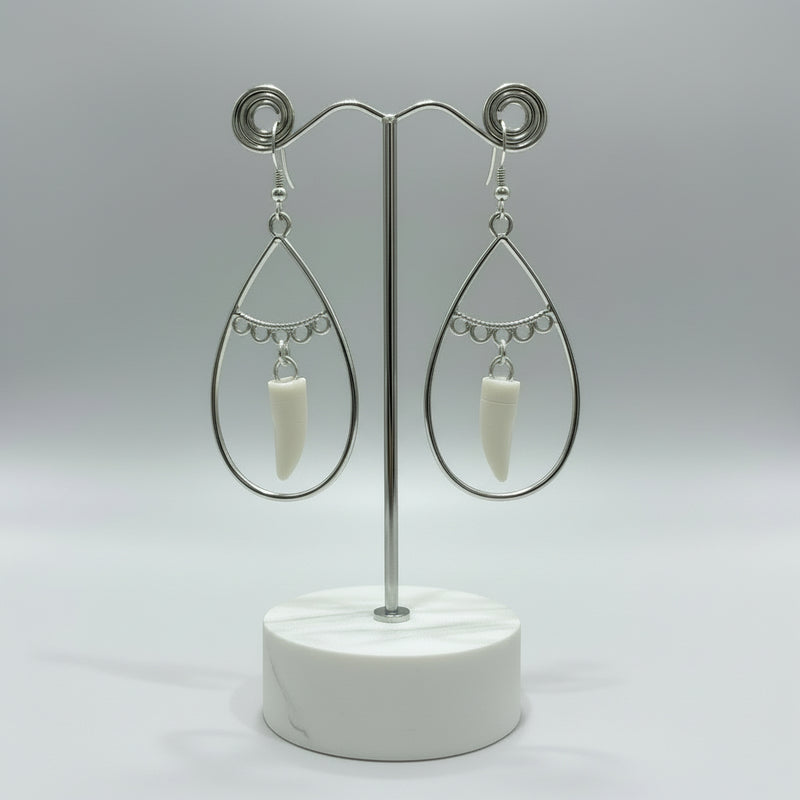 Silver teardrop earrings with white alligator tooth pendants on a blue background