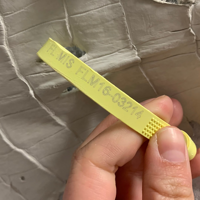 Hand holding a yellow plastic tag with text against a textured background