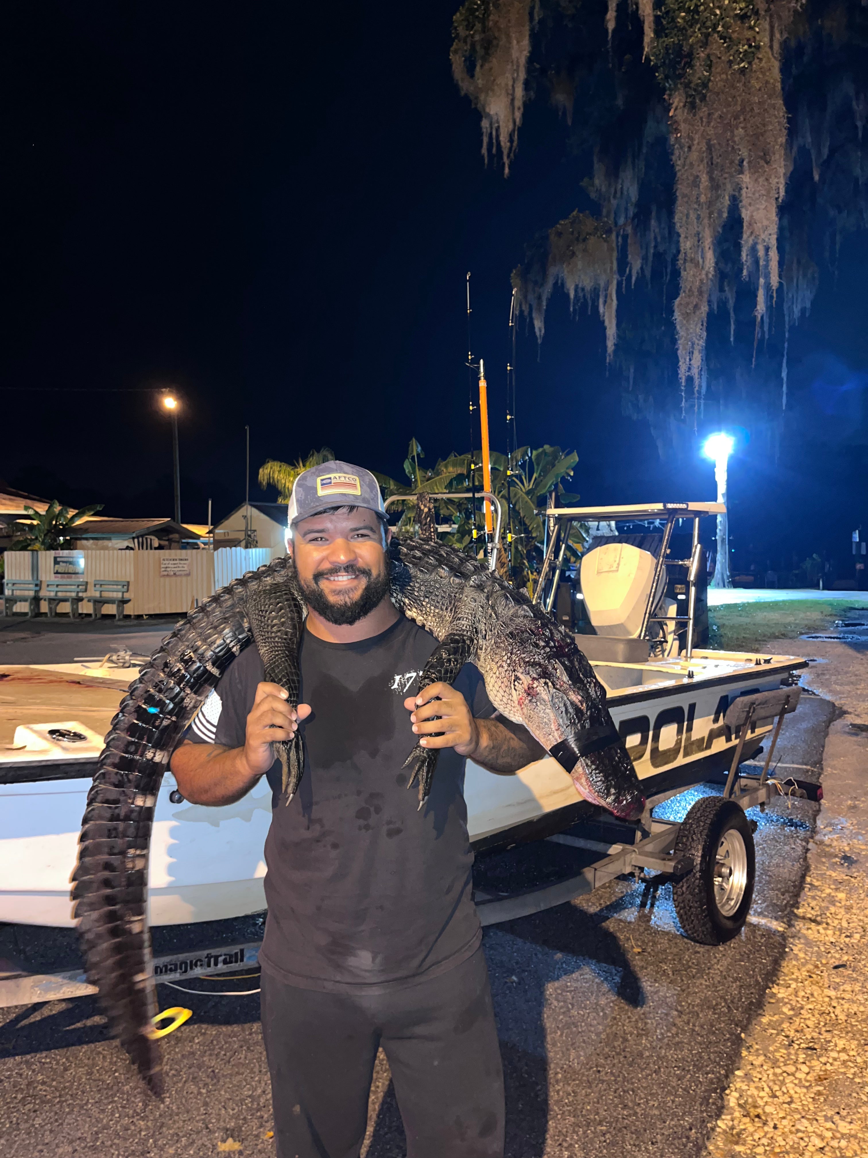 Client holding an alligator near a boat at night.