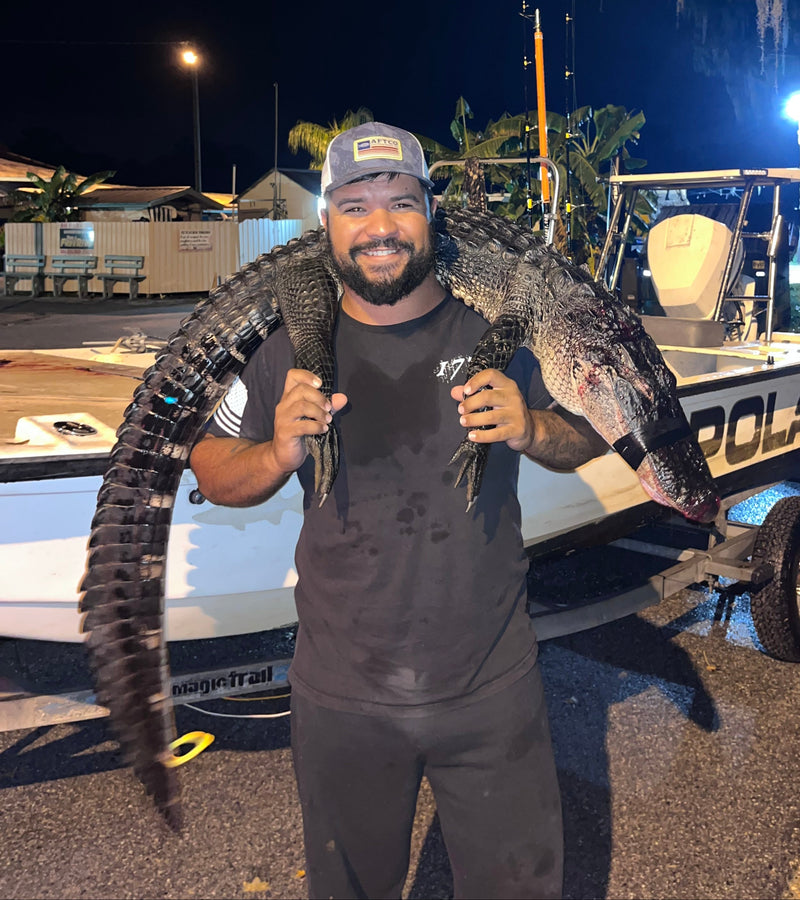 Person holding a large alligator on a street at night
