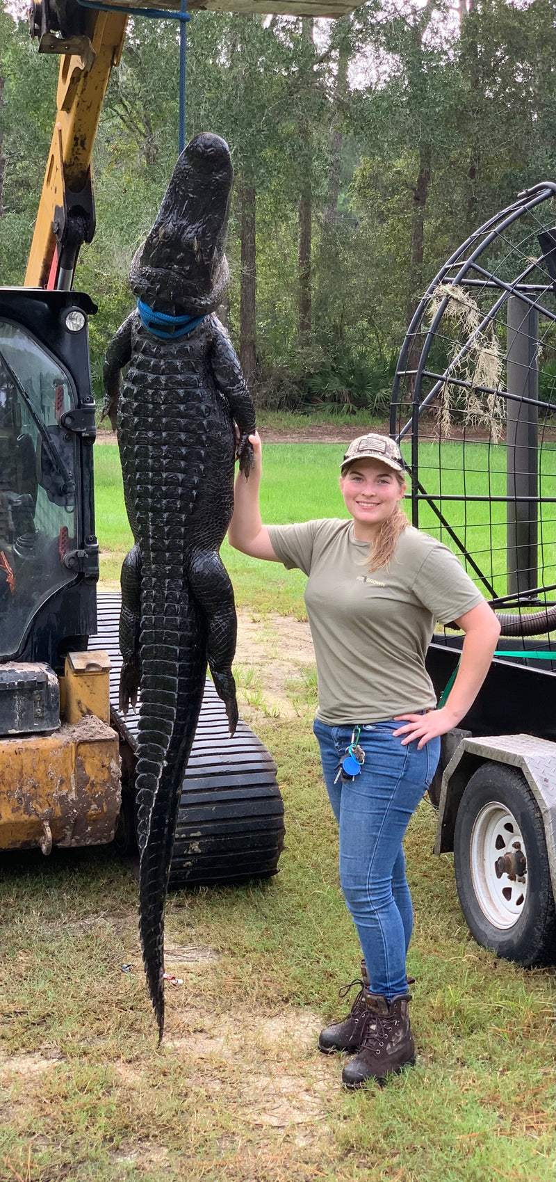 Captain Twigg standing next to 8-foot alligator hoisted up with a tractor next to an airboat