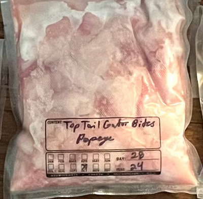 Multiple plastic bags, each containing packaged raw alligator meat with labels indicating the type of cut and weight.