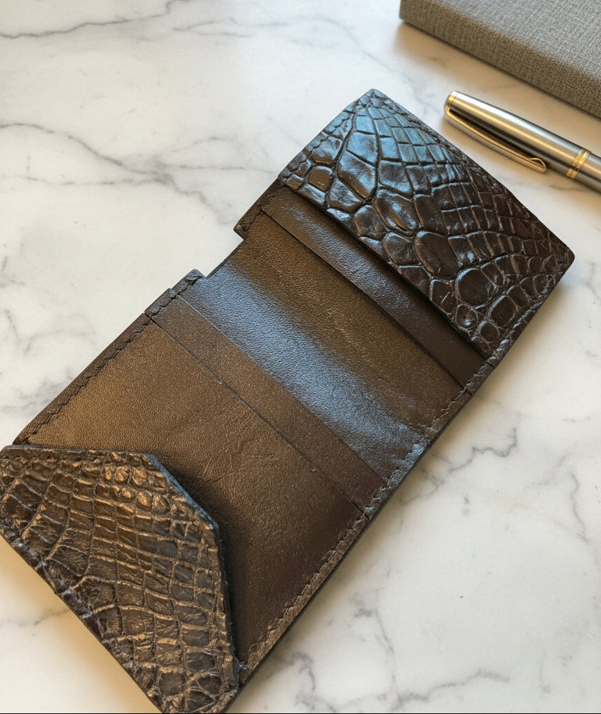 Black alligator skin wallet with leather lining held by a hand, blurred background.