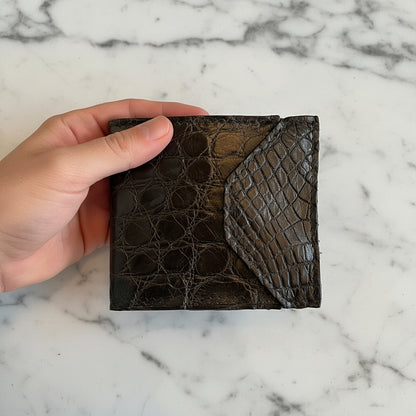 Black alligator skin wallet held by a hand with a blurred background