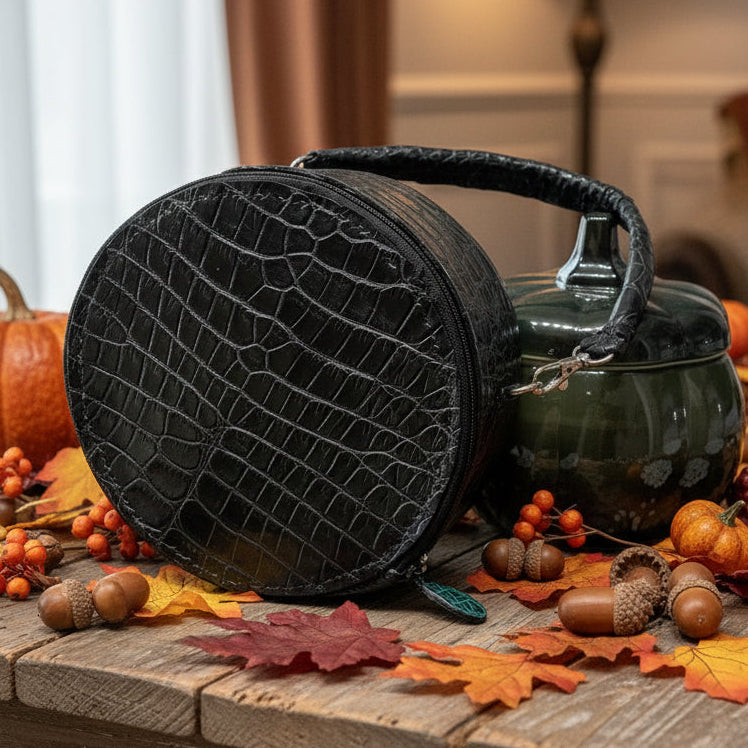 Black round alligator skin bag with a handle.